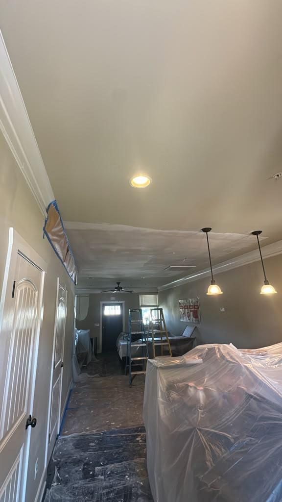 Living room under renovation with plastic-covered furniture, ladder, and hanging light fixtures on ceiling