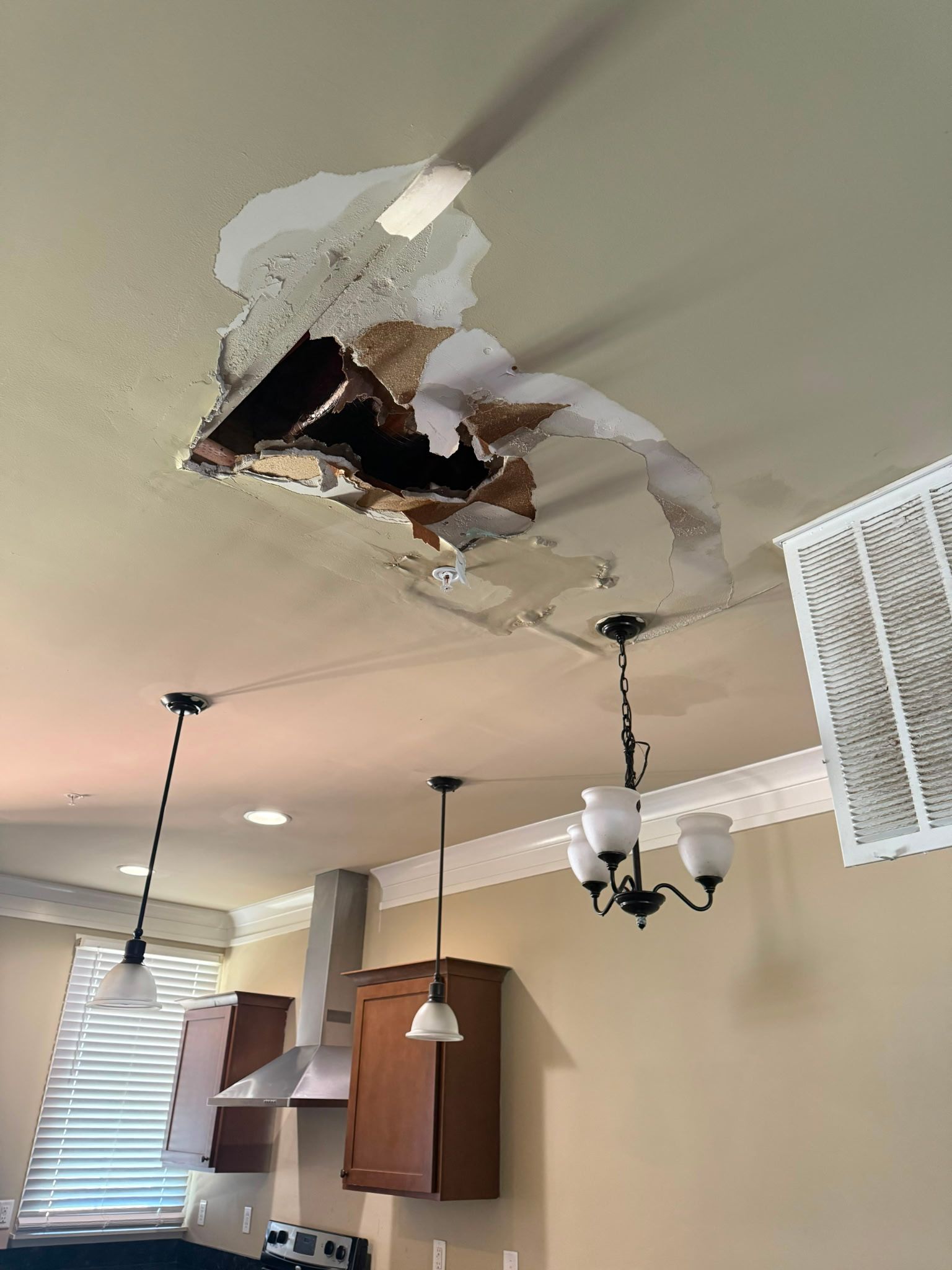 Ceiling damage with a large hole and hanging plaster above a kitchen/dining area