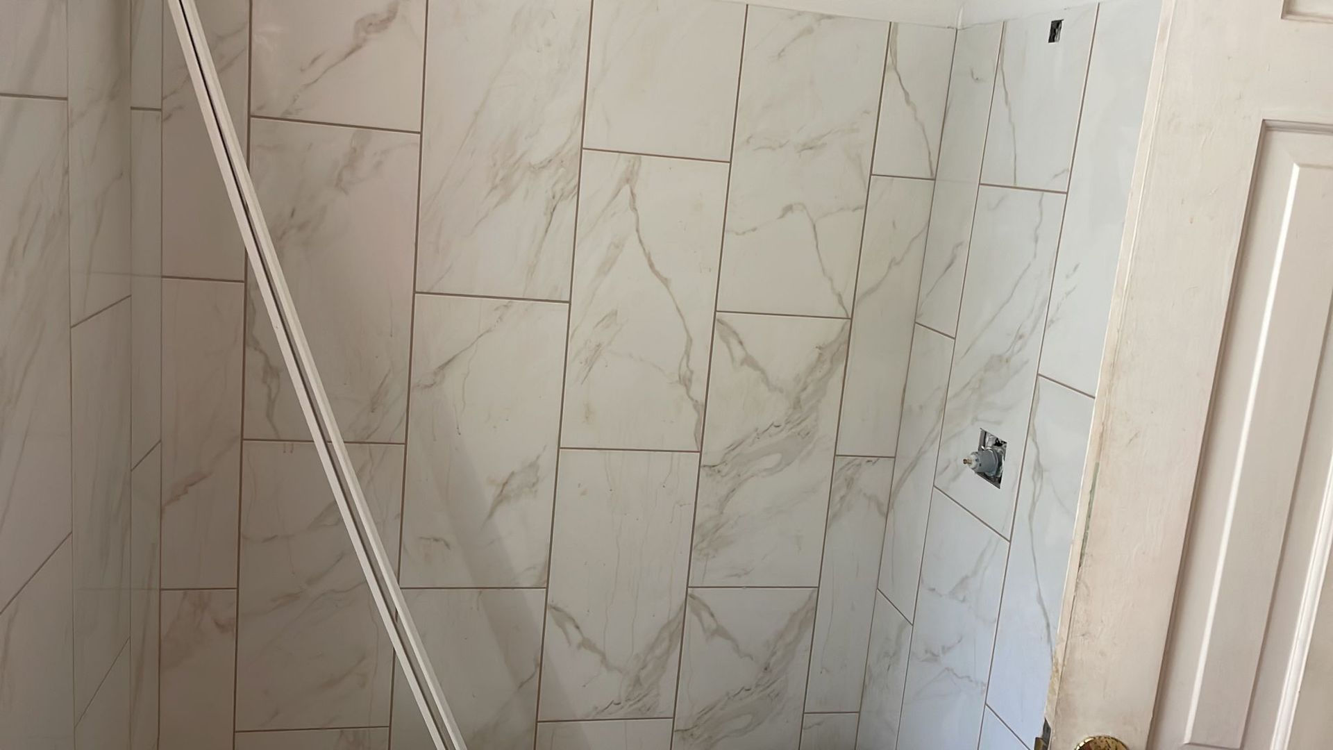 White marble tiled shower walls with a partially installed metal trim piece.