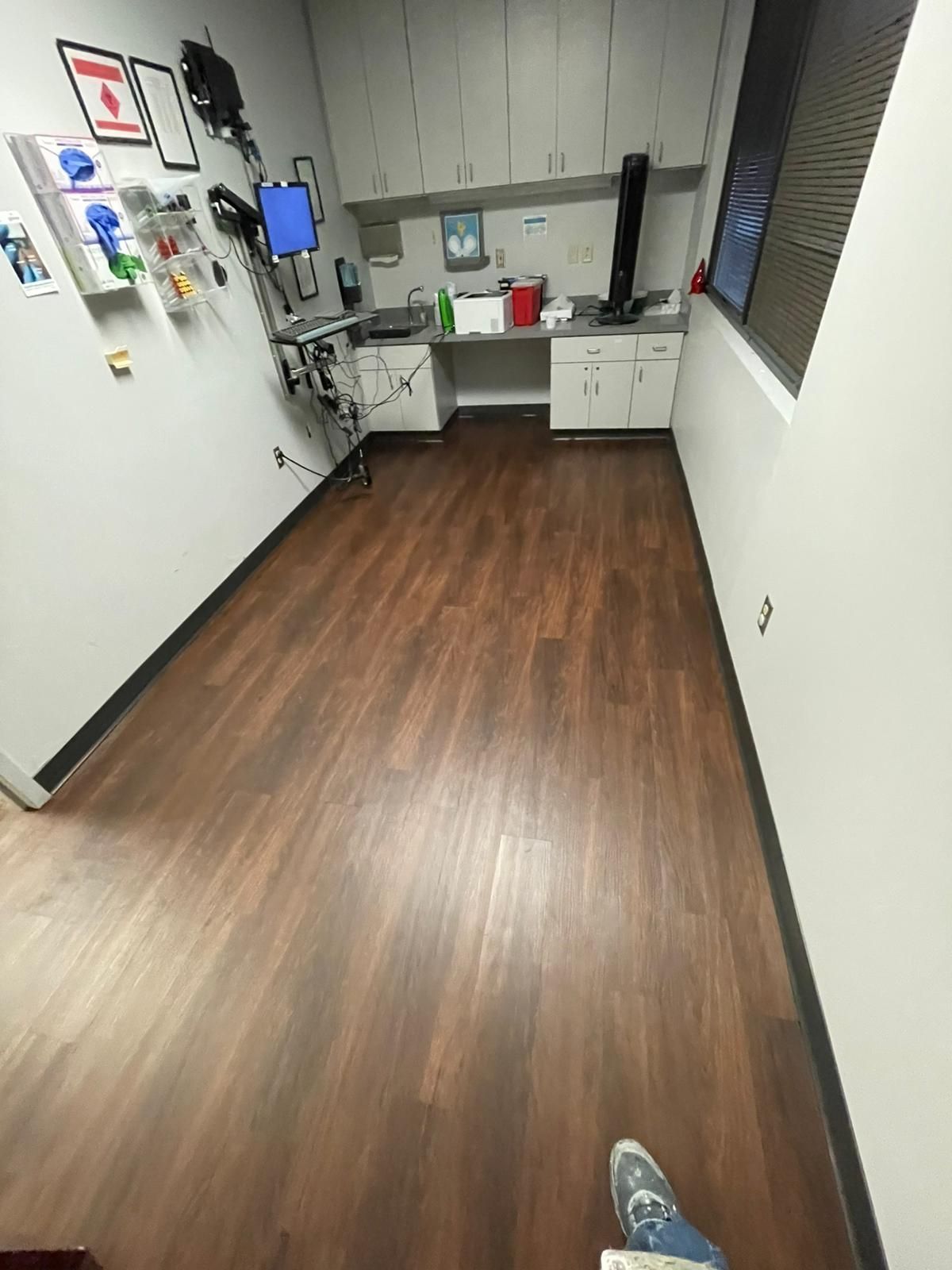 Veterinary examination room with dark wood-look floor, white walls, cabinetry, and equipment.