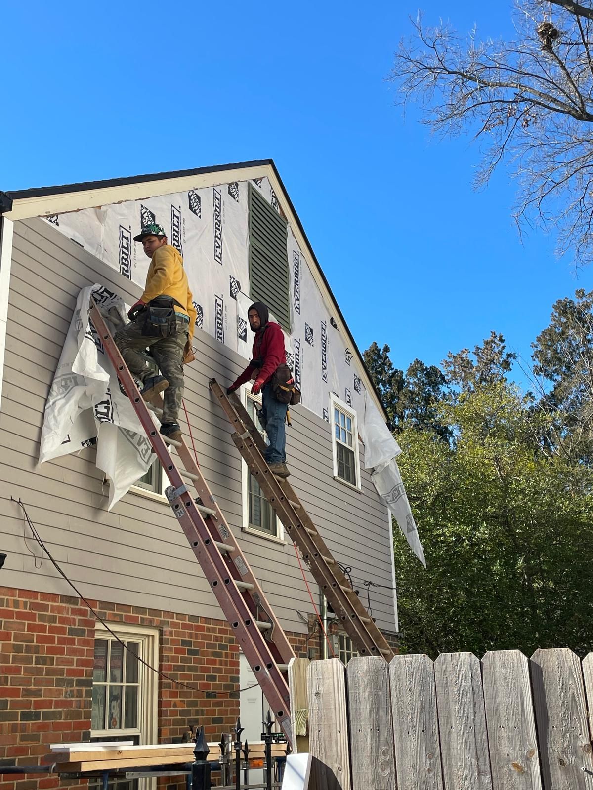 Two workers installing siding on a two-story house, standing on ladders.