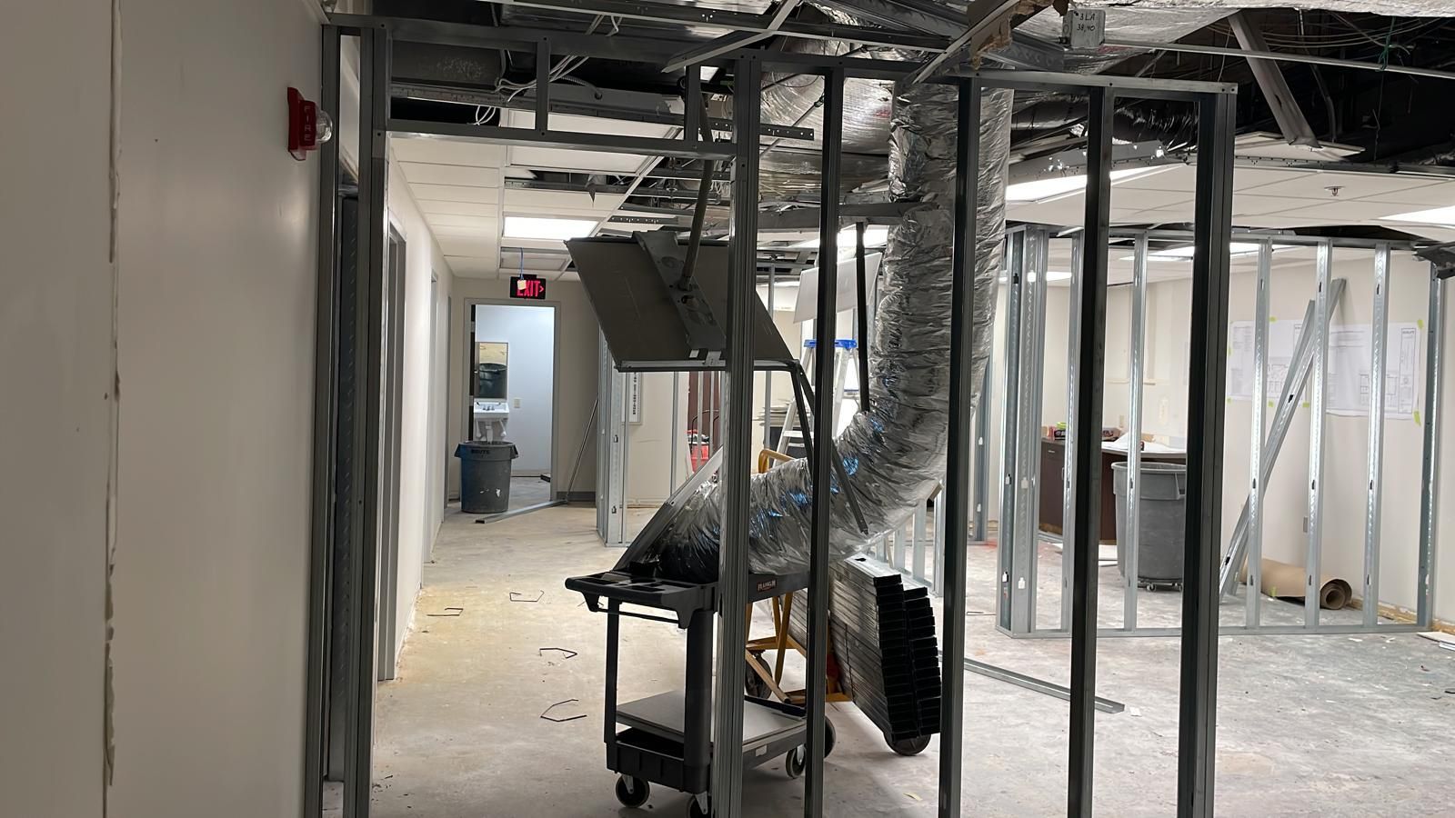 Interior undergoing renovation; metal frames, exposed ductwork, and damaged ceiling visible in the hallway.