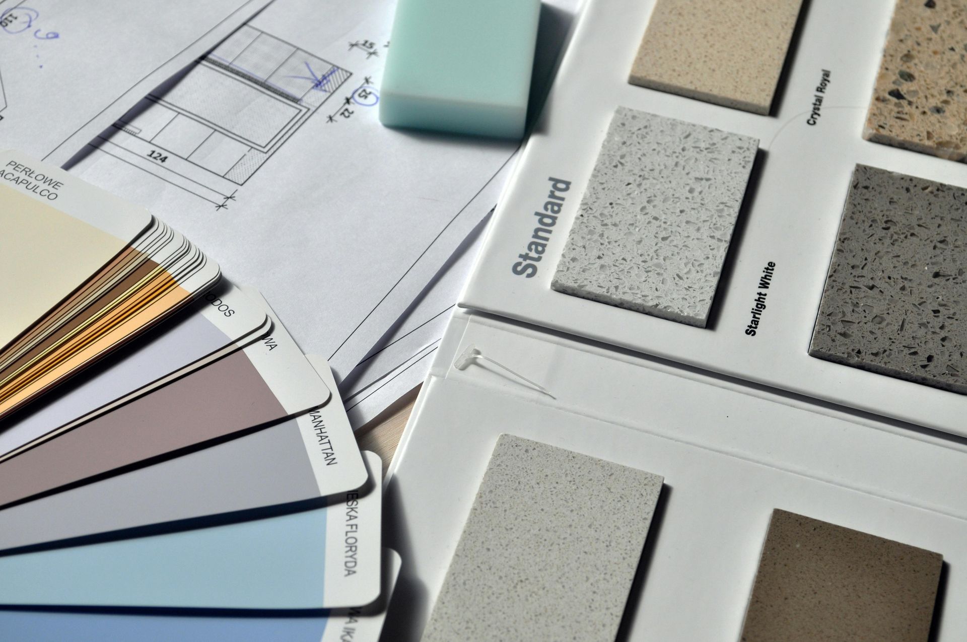 Paint swatches, countertop samples, and architectural plans on a table, showcasing interior design elements.