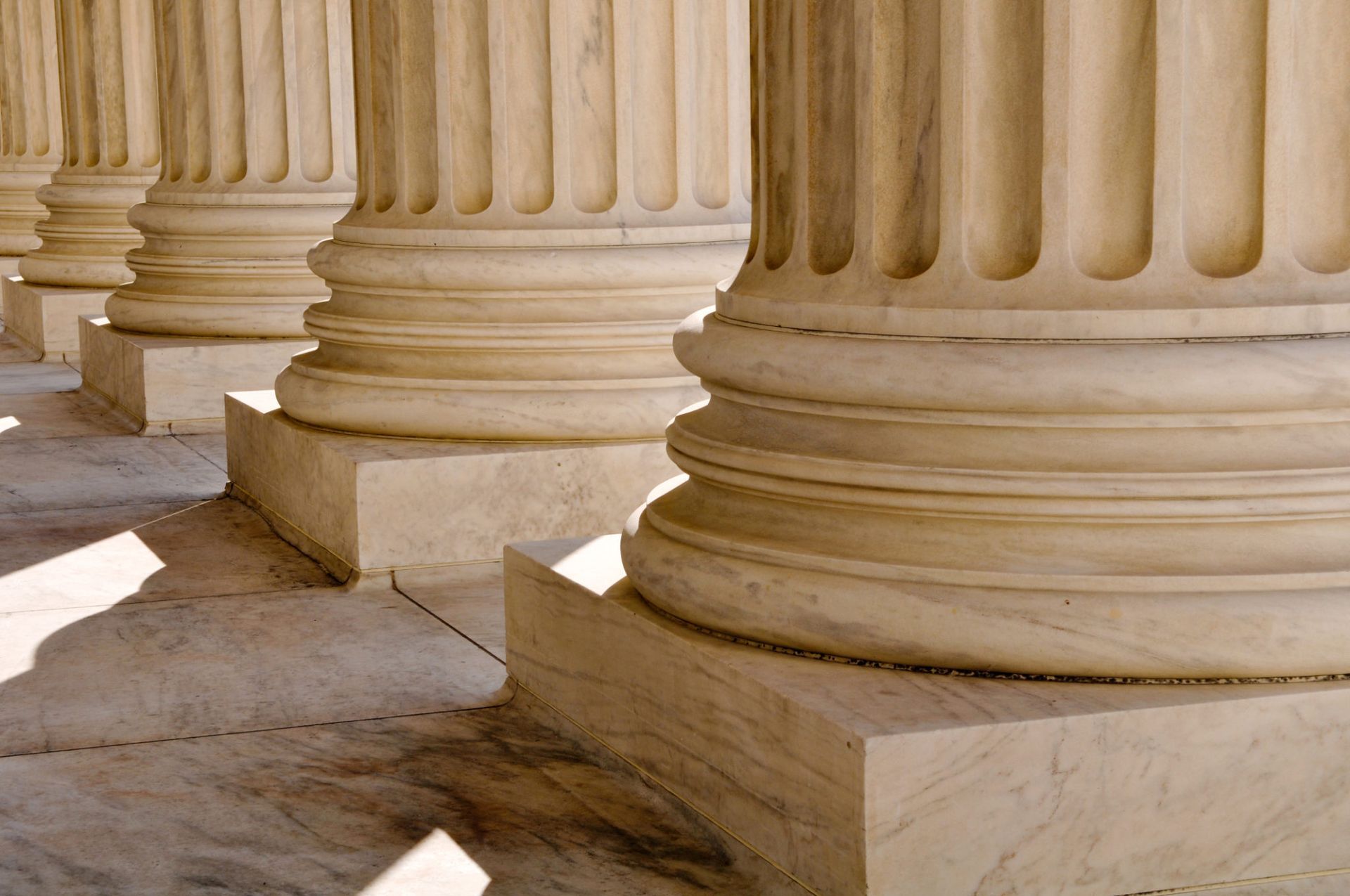 Stone columns in sunlight, with worn bases and shadows on a marble floor