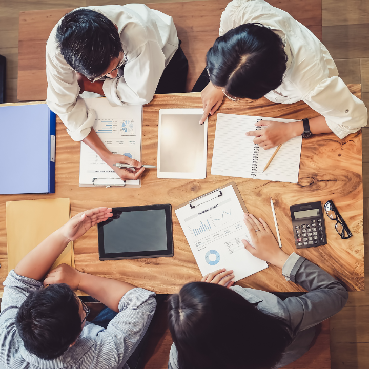 A group of people are sitting around a table with papers and a tablet