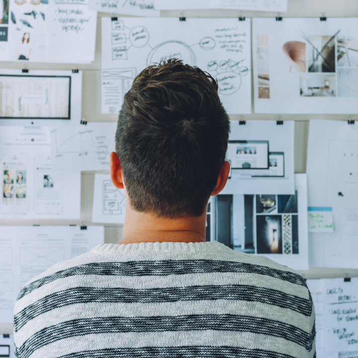 A man in a striped sweater is looking at papers on a wall