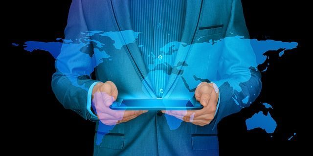 A man in a suit is holding a tablet with a map of the world coming out of it.