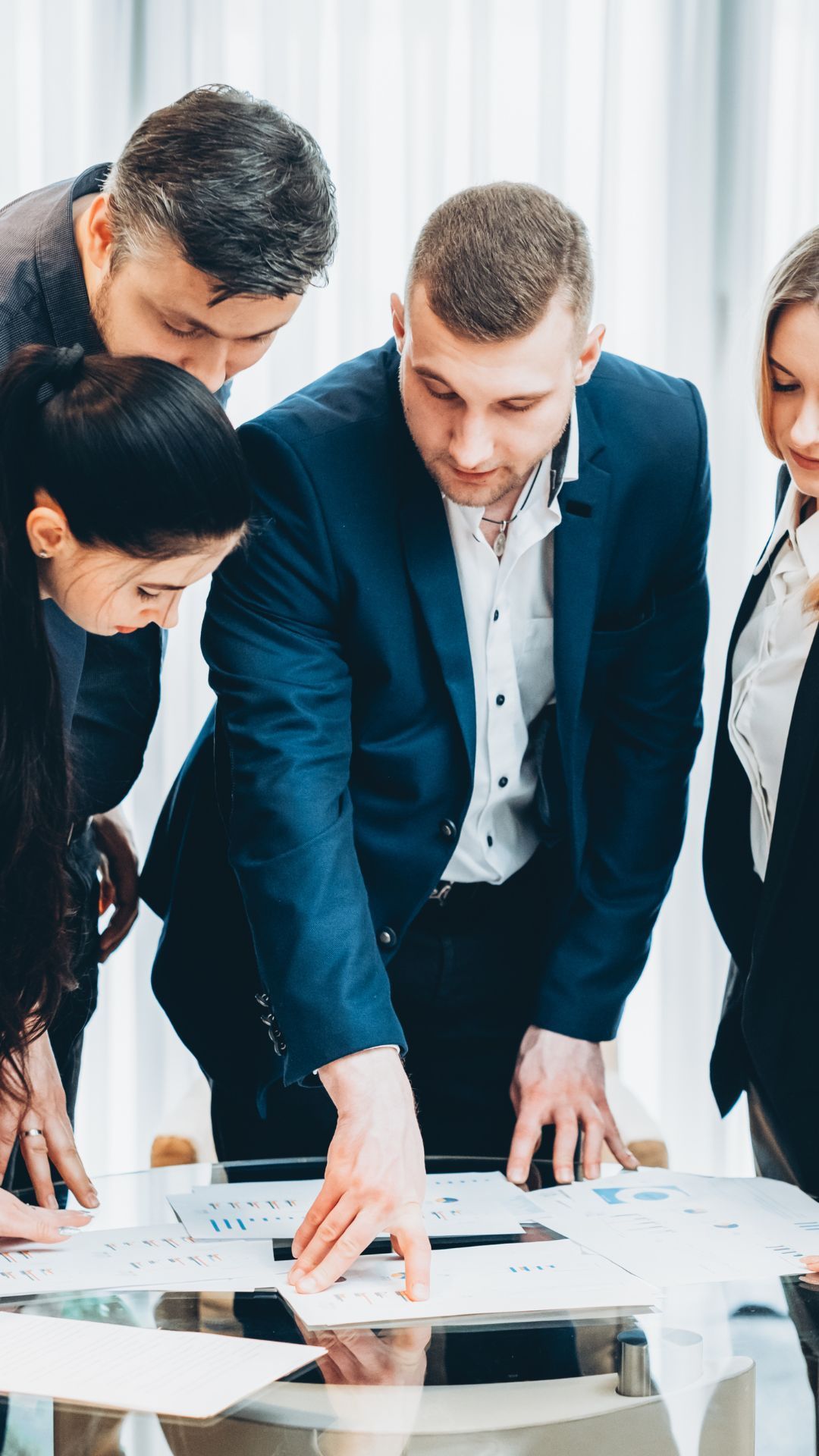A group of business people are standing around a table looking at papers.