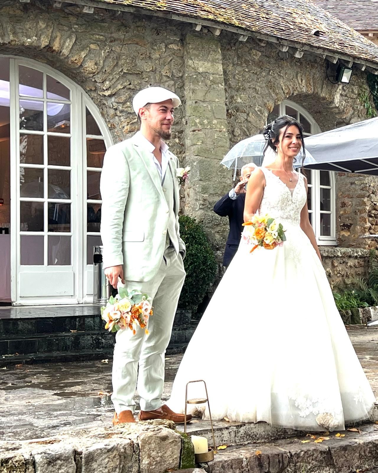 Une mariée et un marié se tiennent devant un bâtiment en pierre tenant des parapluies.