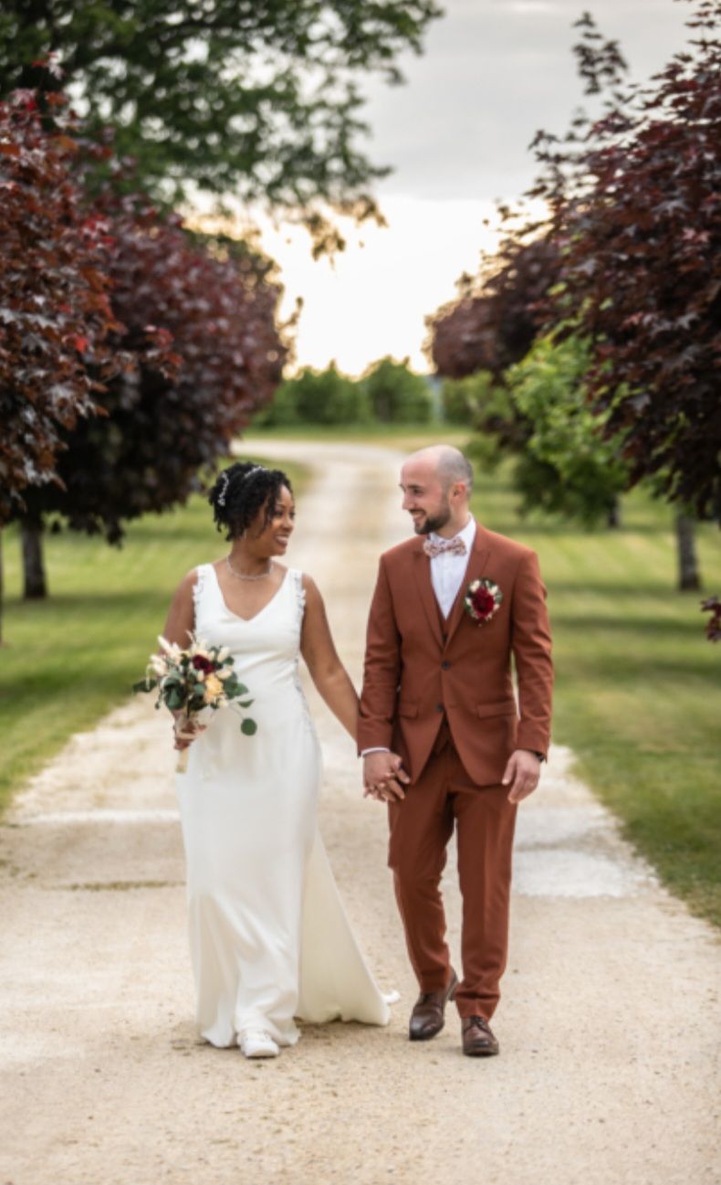 Une mariée et un marié marchent sur un chemin de terre en se tenant la main.