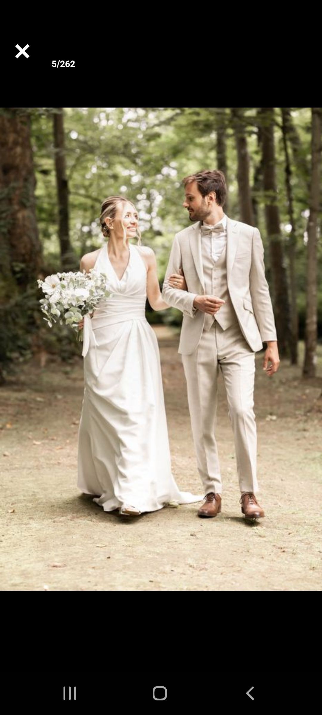 Une mariée et un marié marchent sur un chemin de terre dans les bois.