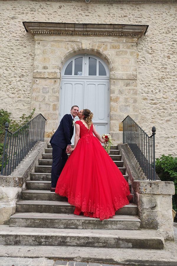 Une mariée et un marié s'embrassent dans les escaliers d'un immeuble. La mariée porte une robe rouge.