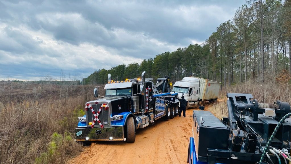 A tow truck is towing a semi truck on a dirt road.