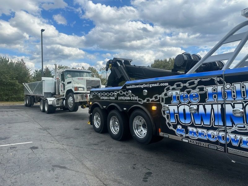 A towing truck is parked next to a dump truck in a parking lot.