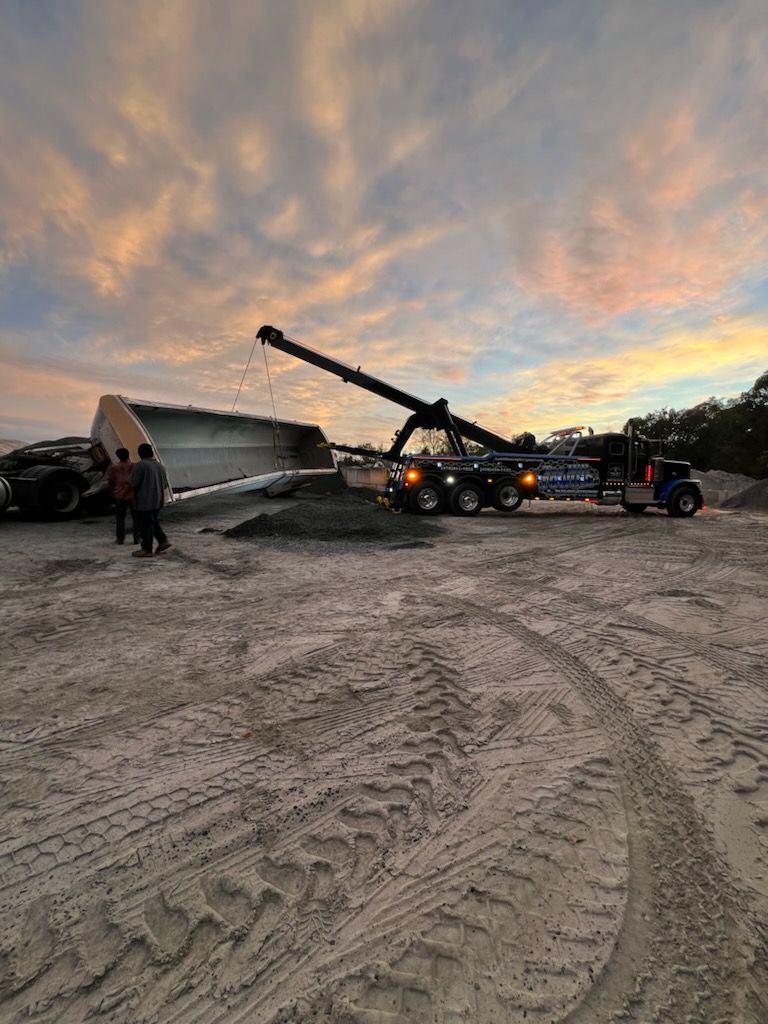 A truck is being towed by a crane in a dirt field.