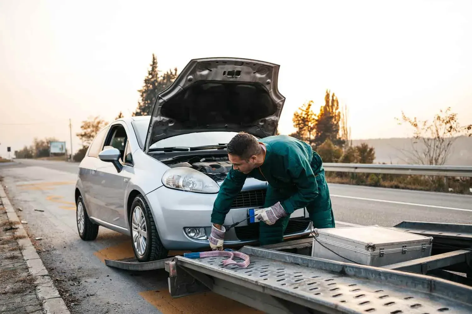 A man is working on a broken down car on the side of the road.