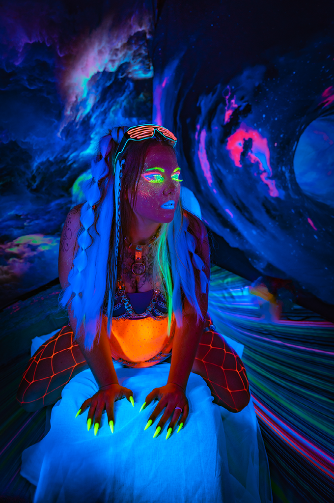A woman is sitting on a bed with glow in the dark paint on her face.