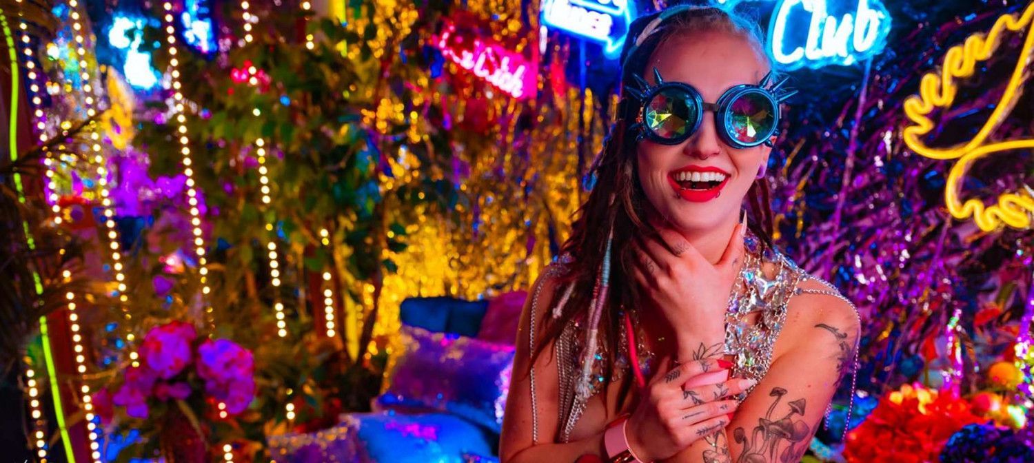 A woman wearing sunglasses and dreadlocks is standing in front of a christmas tree.