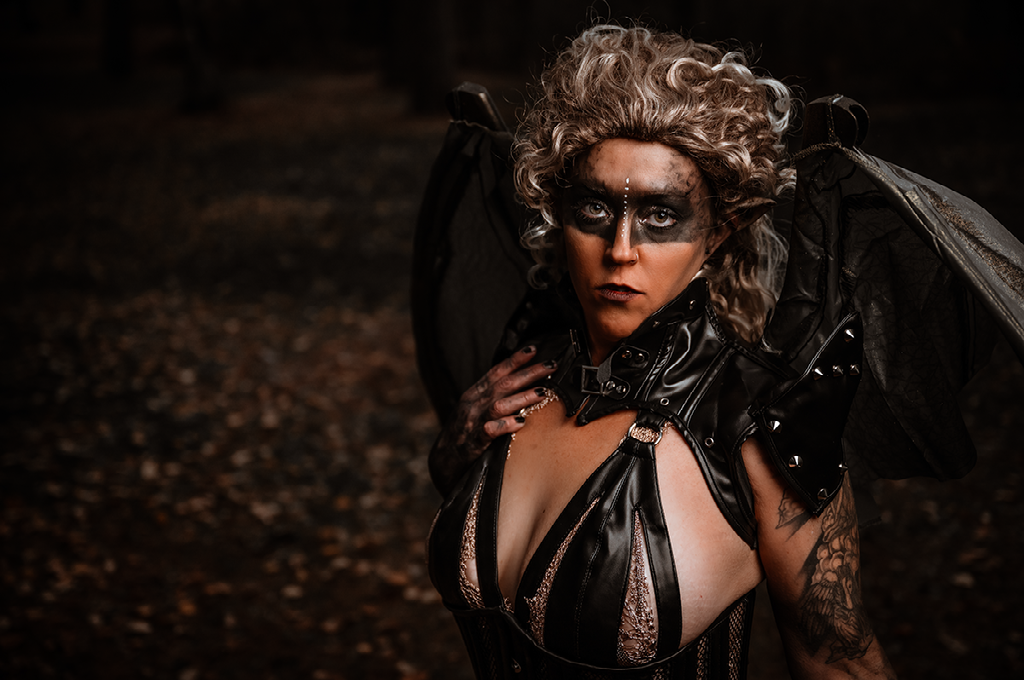 A woman in a black dress with wings is standing in the dark.