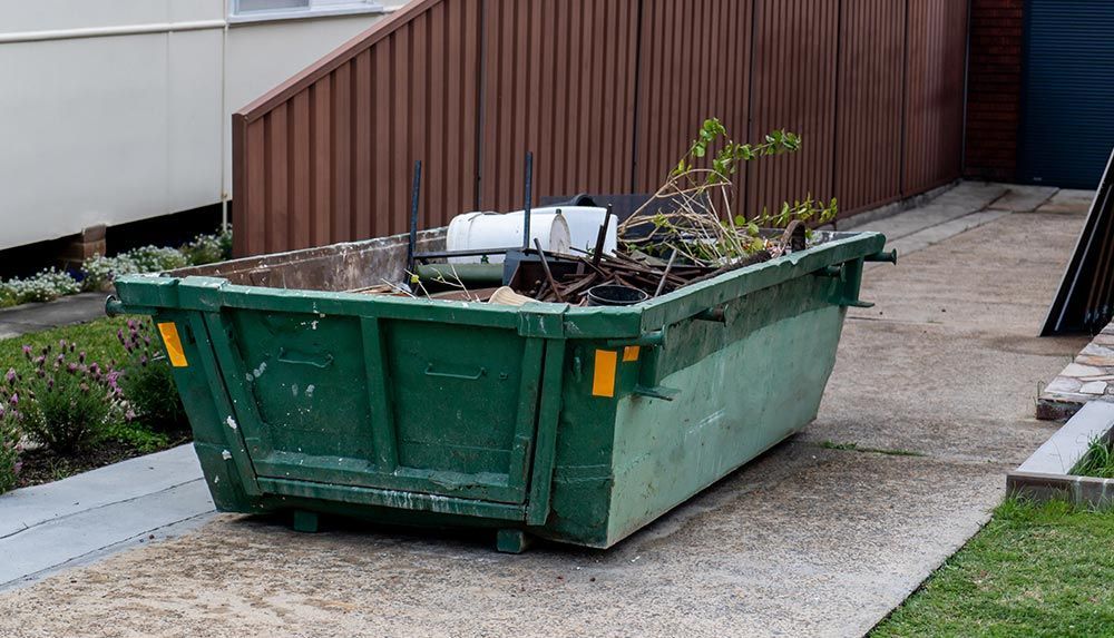 An Abbott Bin Hire skip bin on a residential driveway in Wellington filled with garden waste — residential rubbish removal made easy.