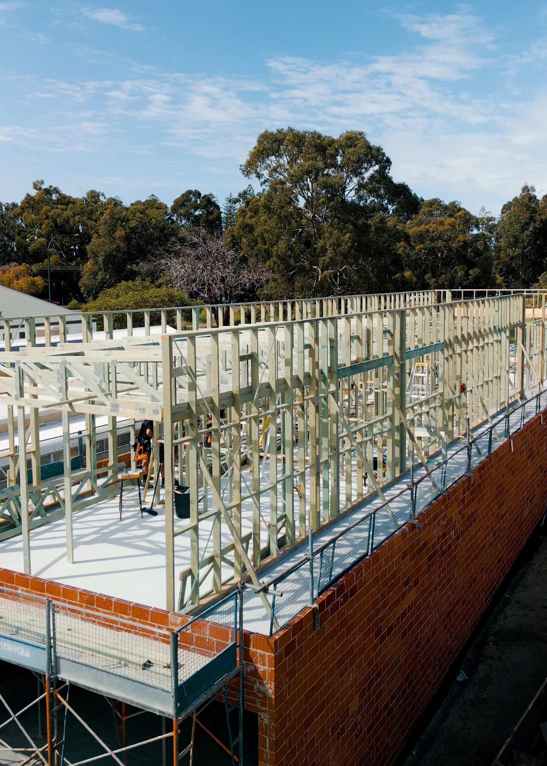 Partially built house frame with exposed studs on a brick foundation under a blue sky
