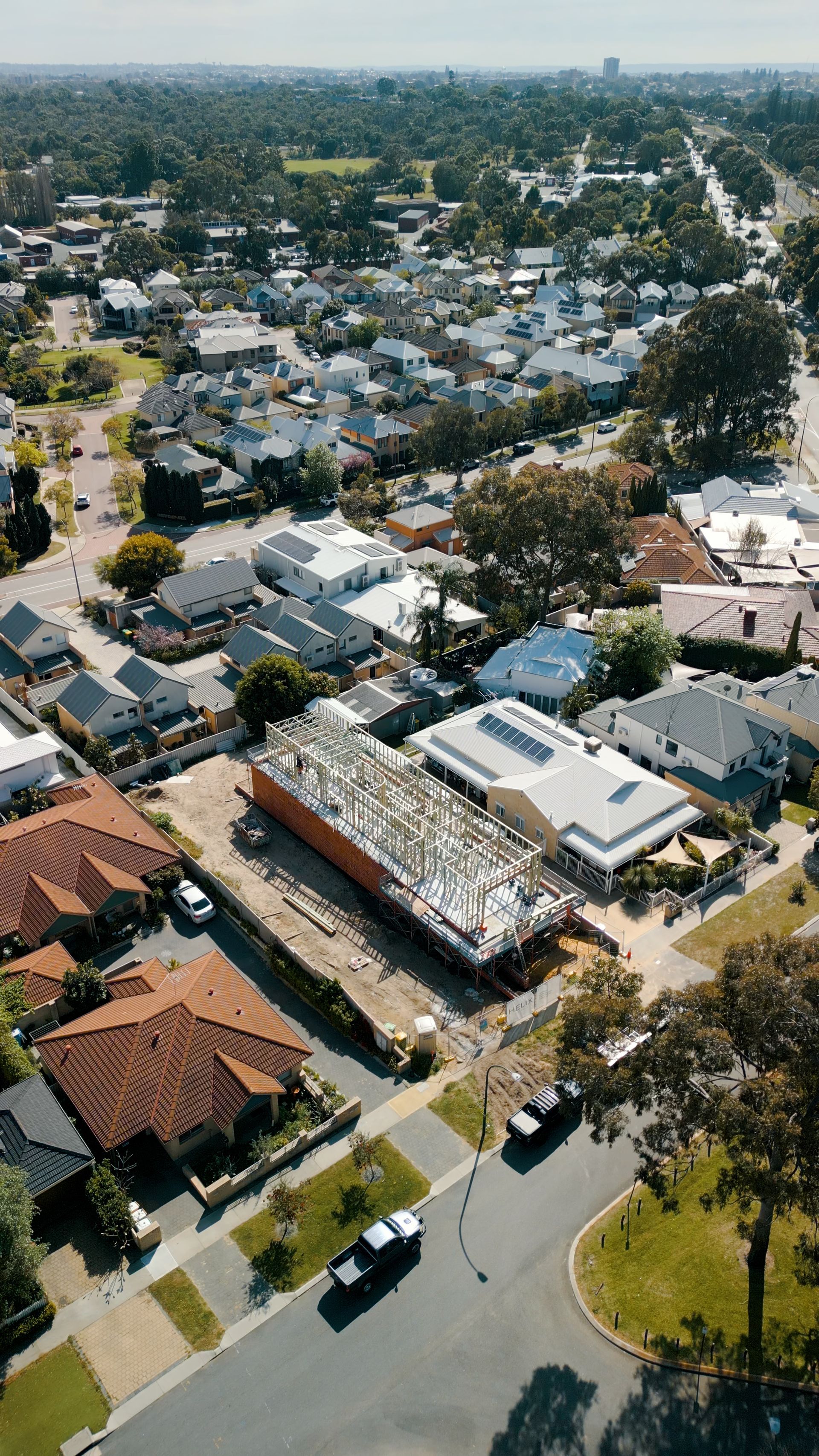 Aerial view of a suburban neighborhood with houses, tree-lined streets, and a distant city skyline.