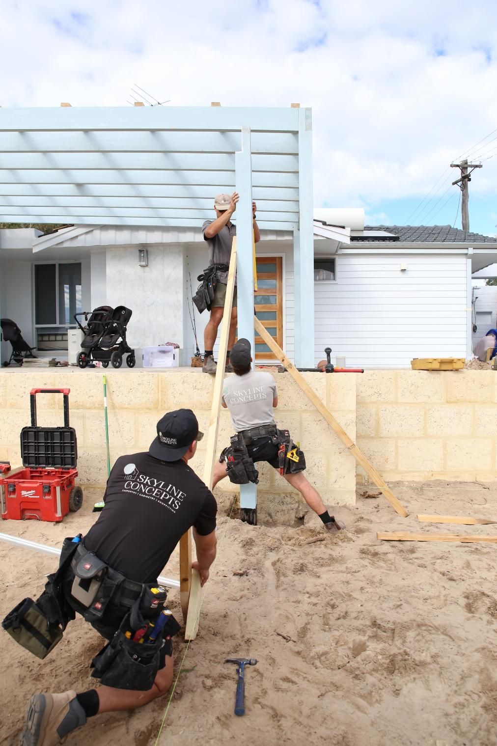 Police officers use a ram in a sandy training area beside a house