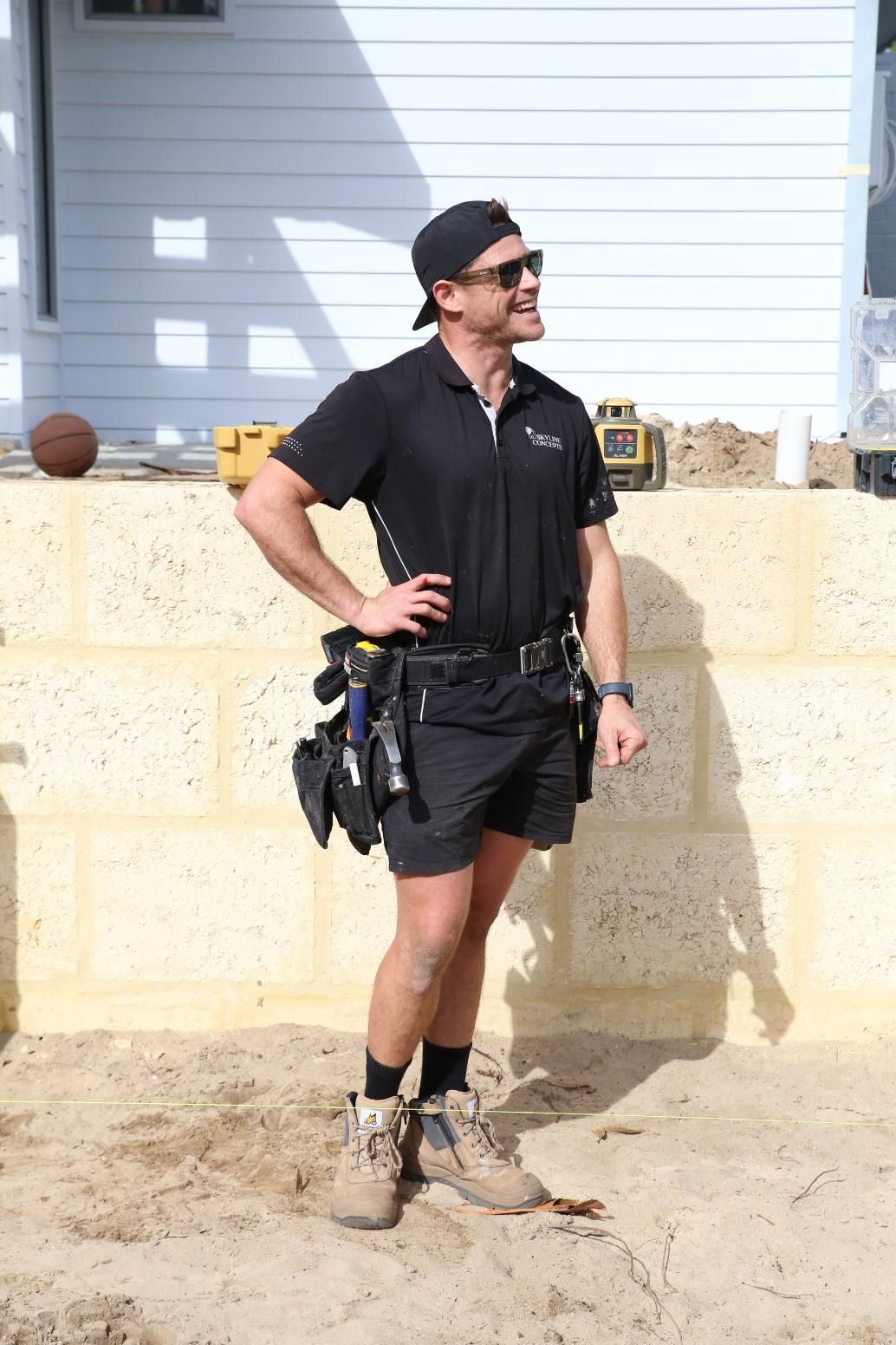 Worker pointing at house under construction with exposed roof framing and steps in front