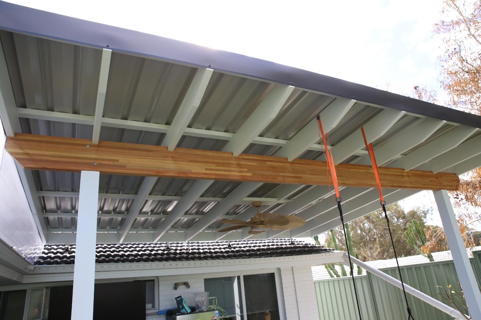 Covered carport with exposed beams and orange straps, viewed from below next to a house.