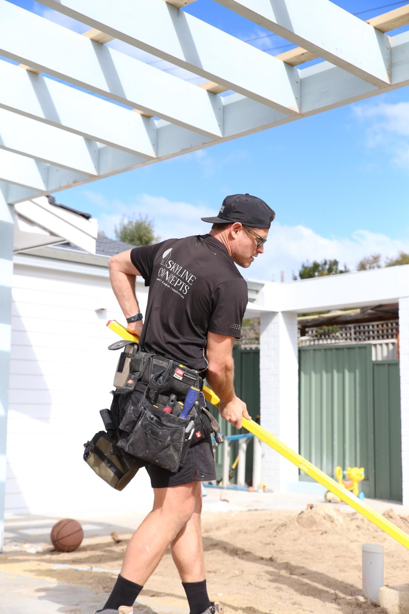 Worker in black clothes carrying a yellow hose on a construction site under a white pergola