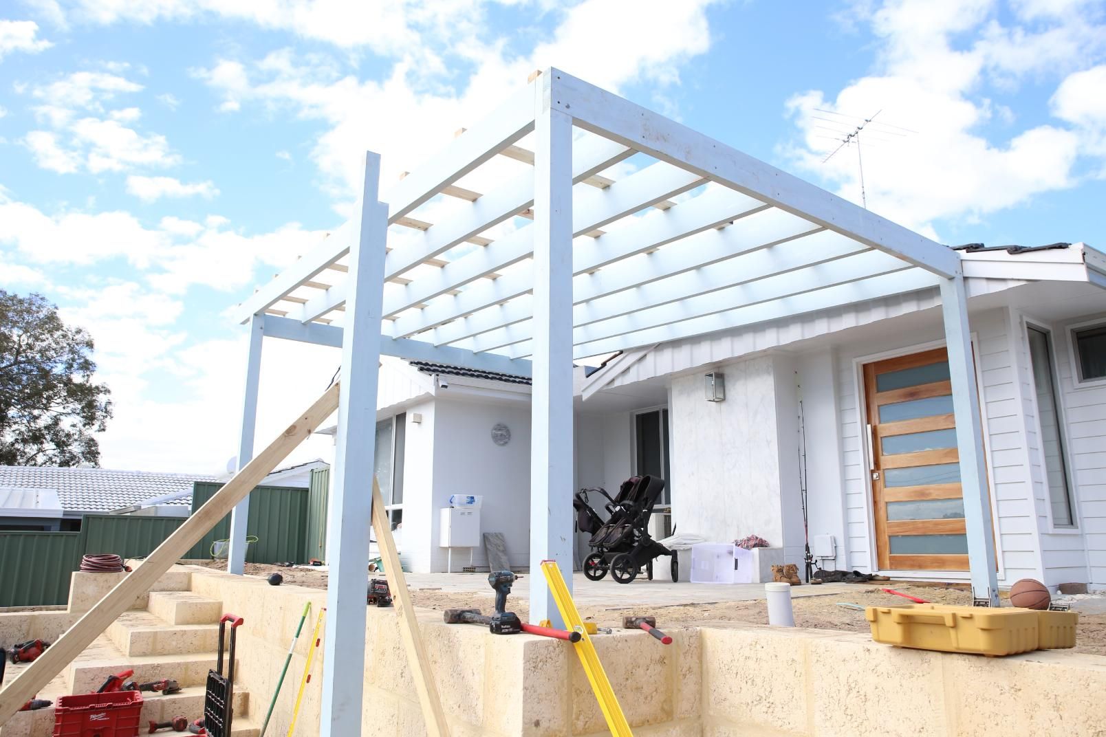Construction site with a white house patio frame, stairs, and building materials under a blue sky