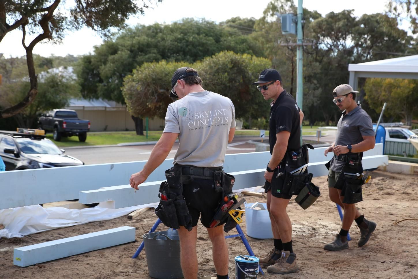 Three workers in hard hats assembling white foam blocks at an outdoor construction site.