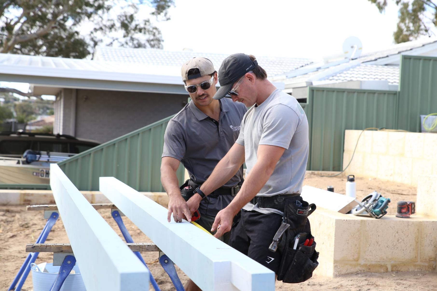 Two workers measuring white beams outdoors at a construction site