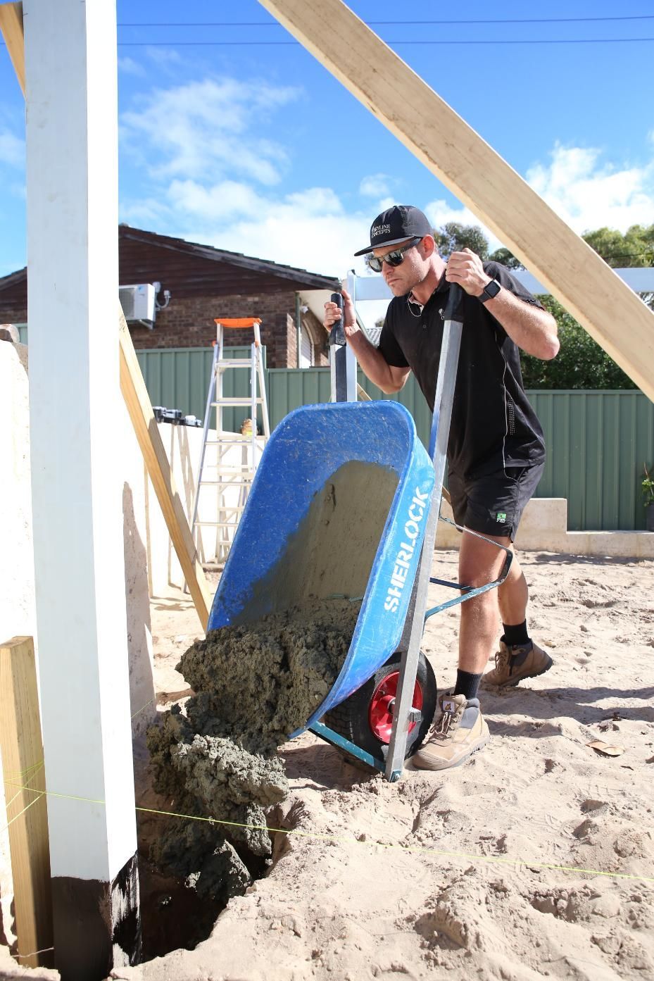Worker shoveling wet concrete from a blue wheelbarrow at a construction site