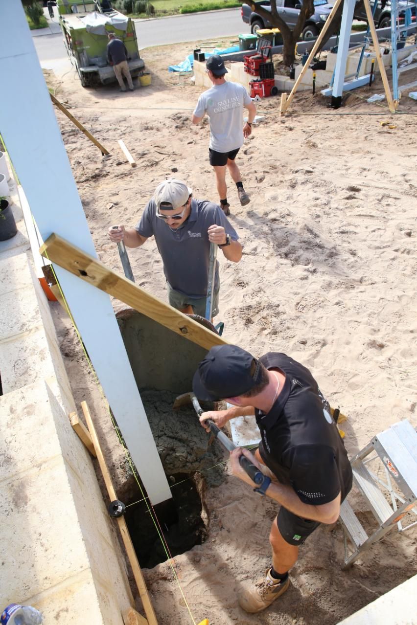 People climbing a sandy trench beside a metal structure at an outdoor construction site