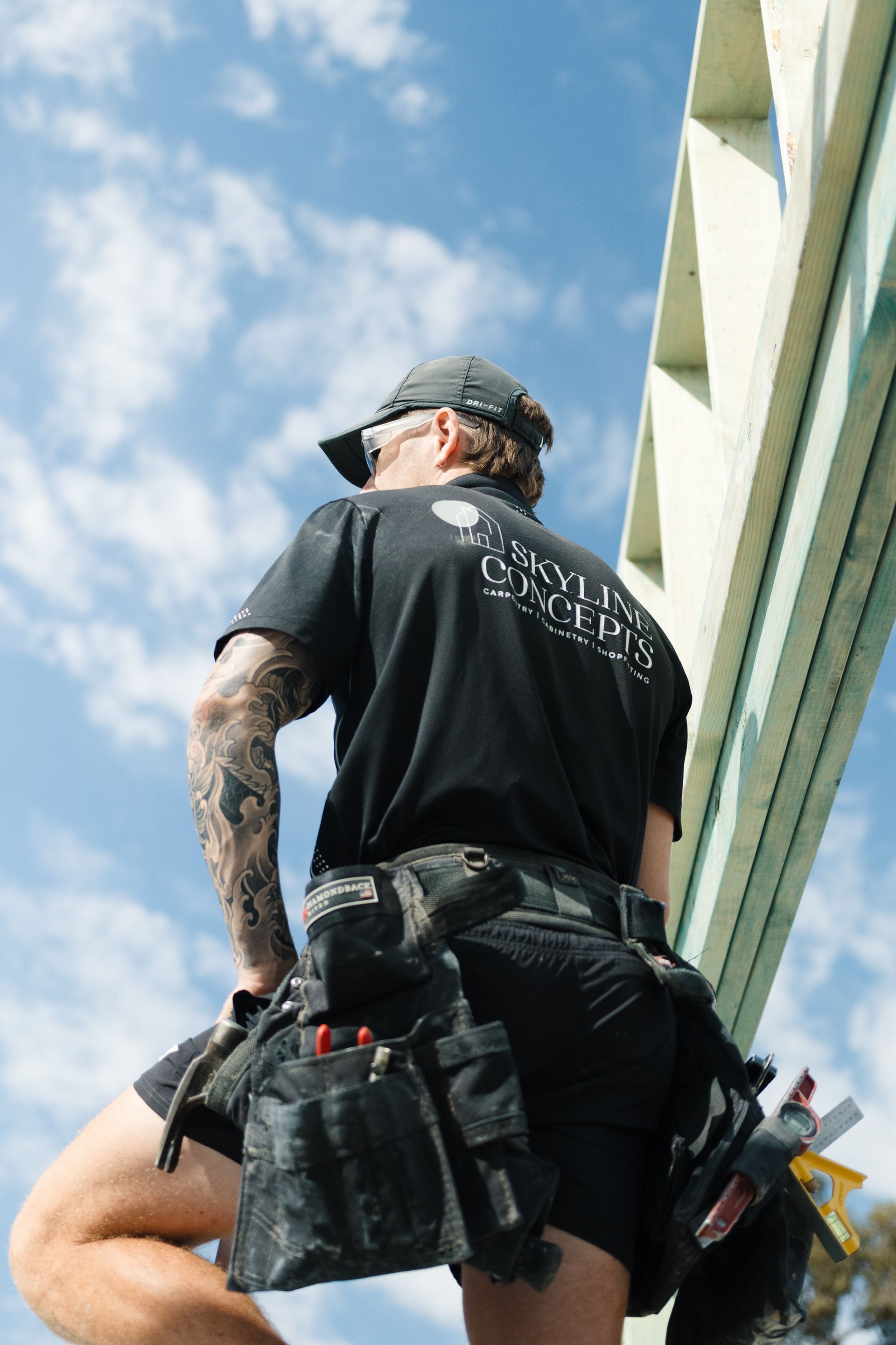 Person in black workwear and safety harness climbing beside a building against a blue sky