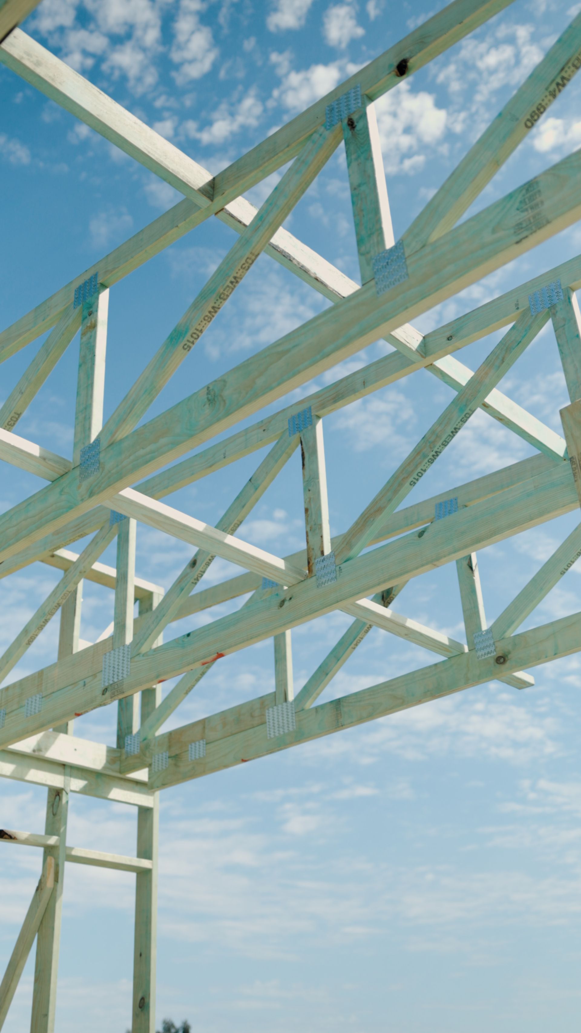 White wooden roof trusses against a blue sky with scattered clouds