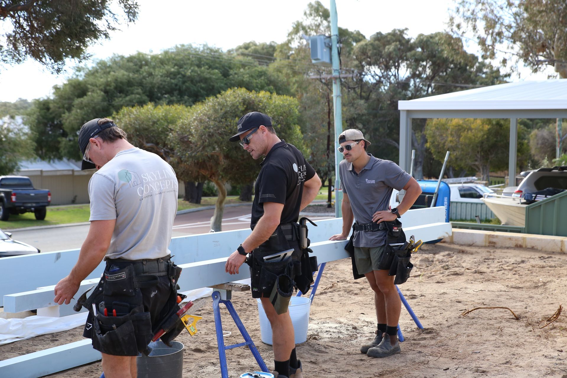 Three workers in safety gear assemble a light-blue structure outdoors near a white tent.