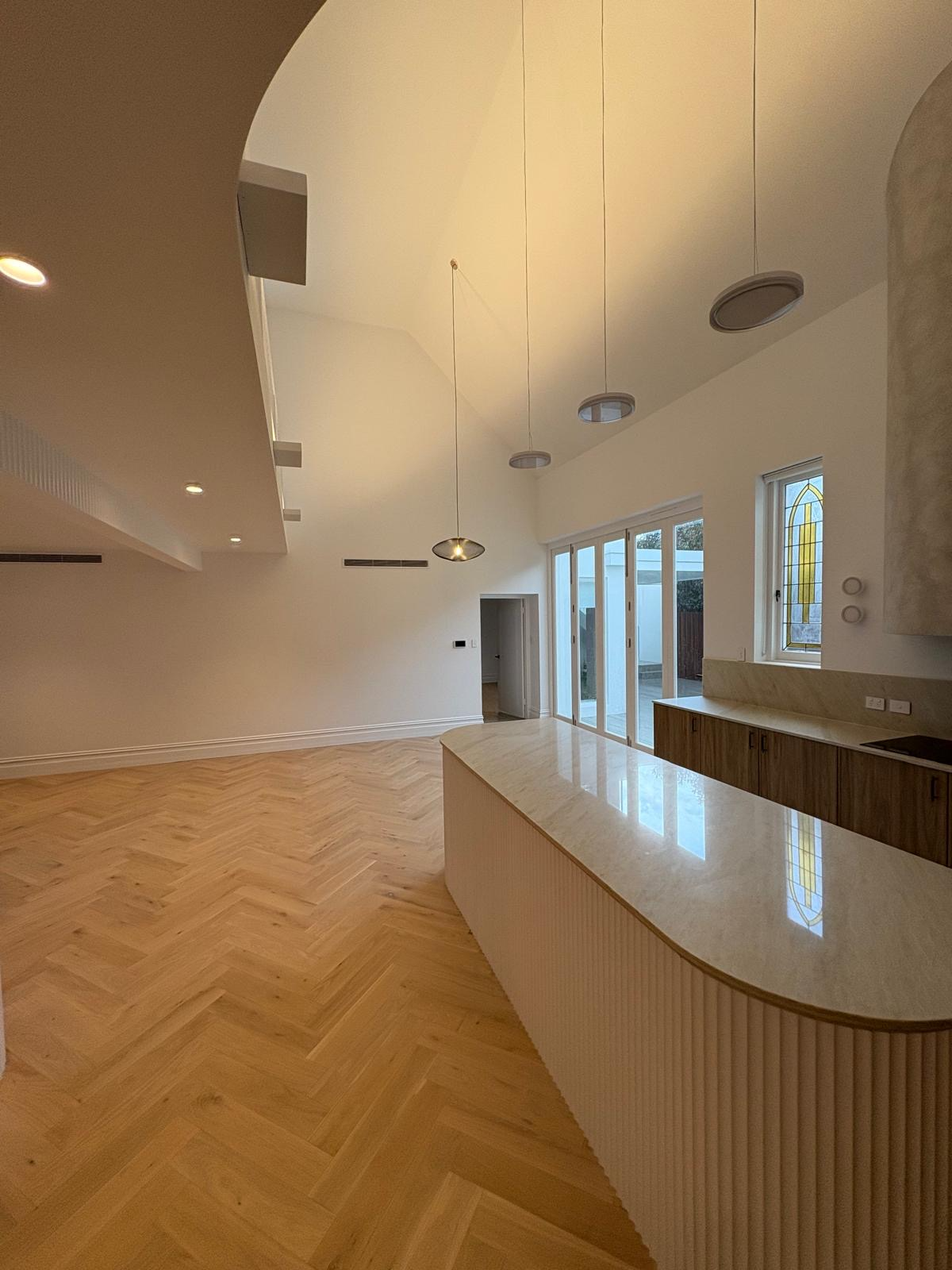 Bright modern room with herringbone wood floor, curved counter, pendant lights, and large windows with city view