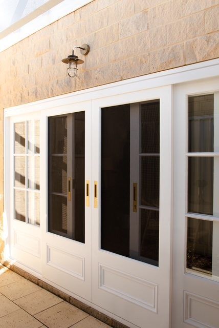 White double glass doors with brass handles beneath a wall-mounted lantern on a stone exterior wall.