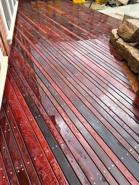 Rain-soaked red wooden deck boards with water puddles, stone wall at right, and white railing at left