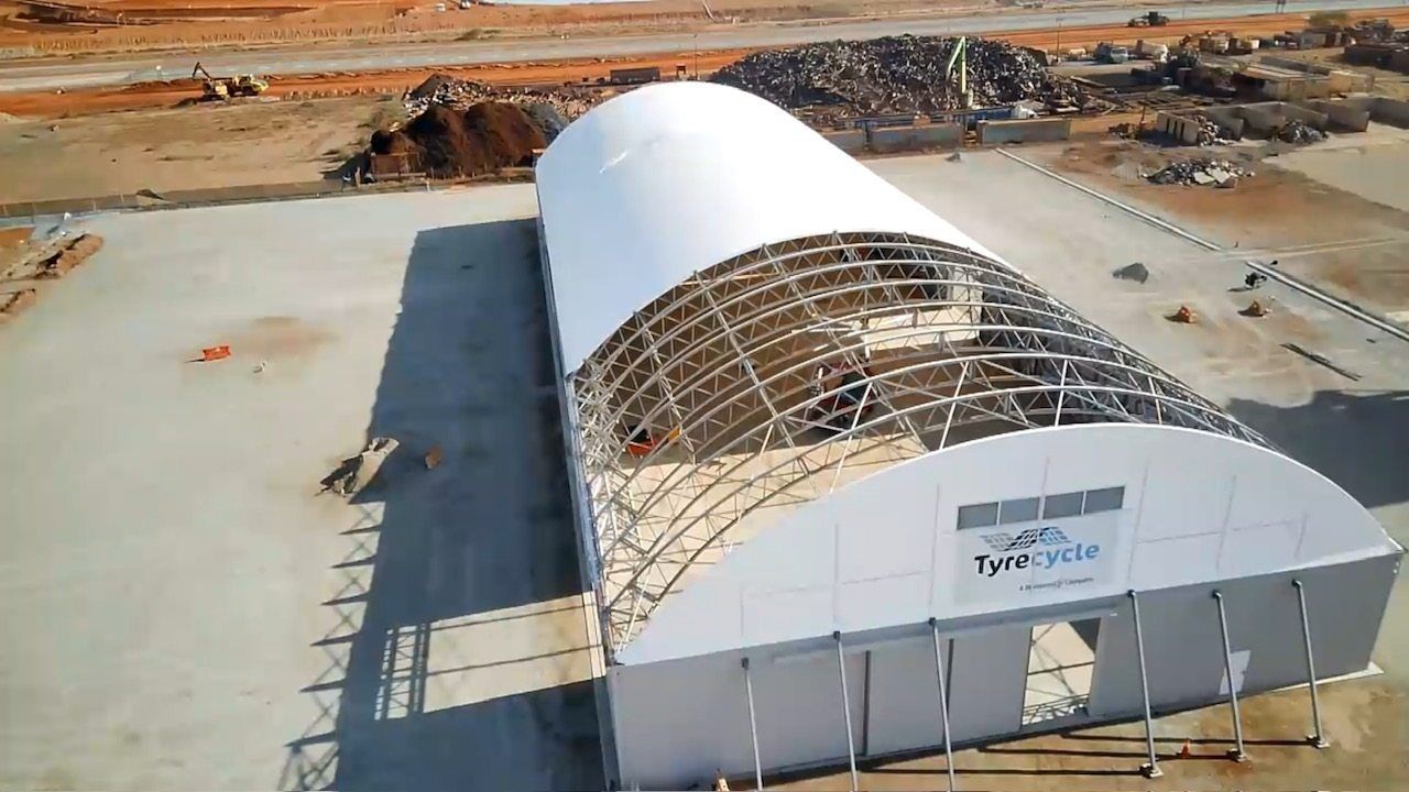 Aerial view of a large white arched building under construction on a dusty industrial site.