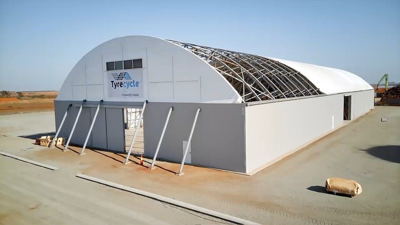 White tent-like industrial building with open roof frame in a desert setting