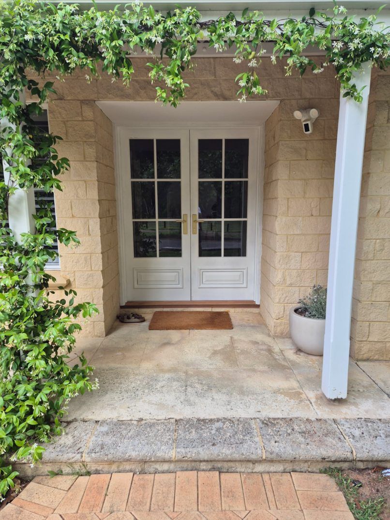 Stone porch with white double doors, ivy overhead, and a potted plant beside the entrance