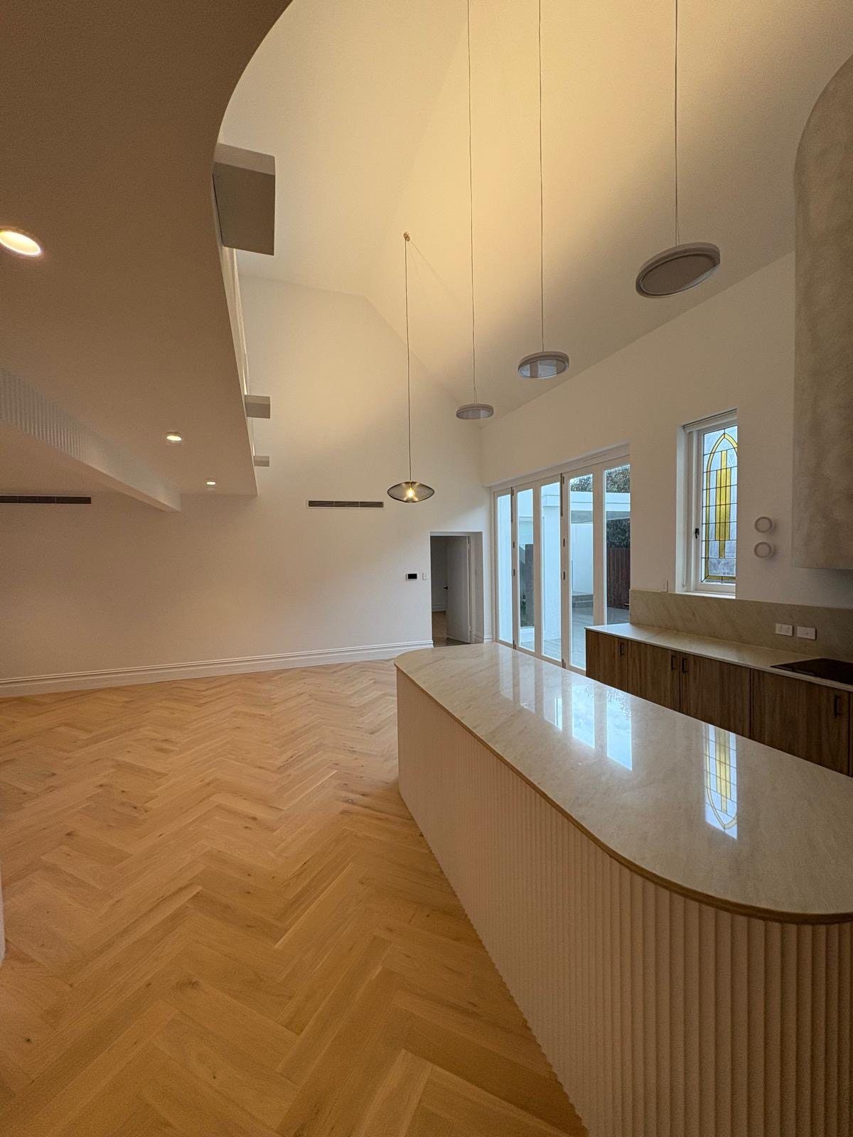 Bright modern gallery with herringbone wood floor, curved white ceiling, and a long reception counter by large windows