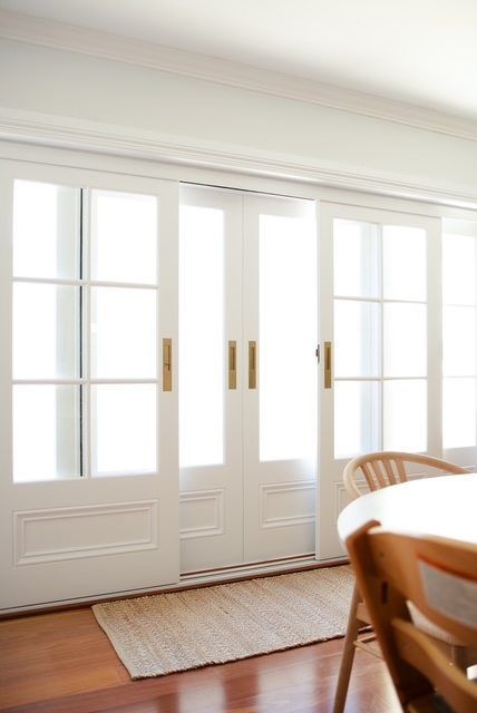 Bright white French doors with sidelights in a dining room, beside a wooden table and chairs.