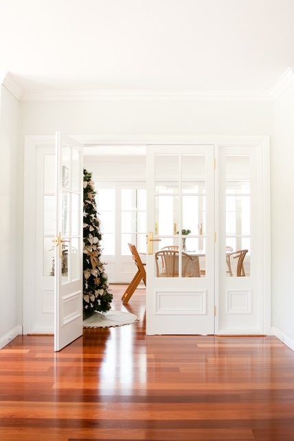 Bright white dining room with open French doors, wooden floors, and a decorated table near a Christmas tree.