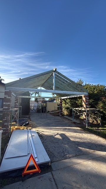 Partially built metal carport frame on a driveway under a clear blue sky