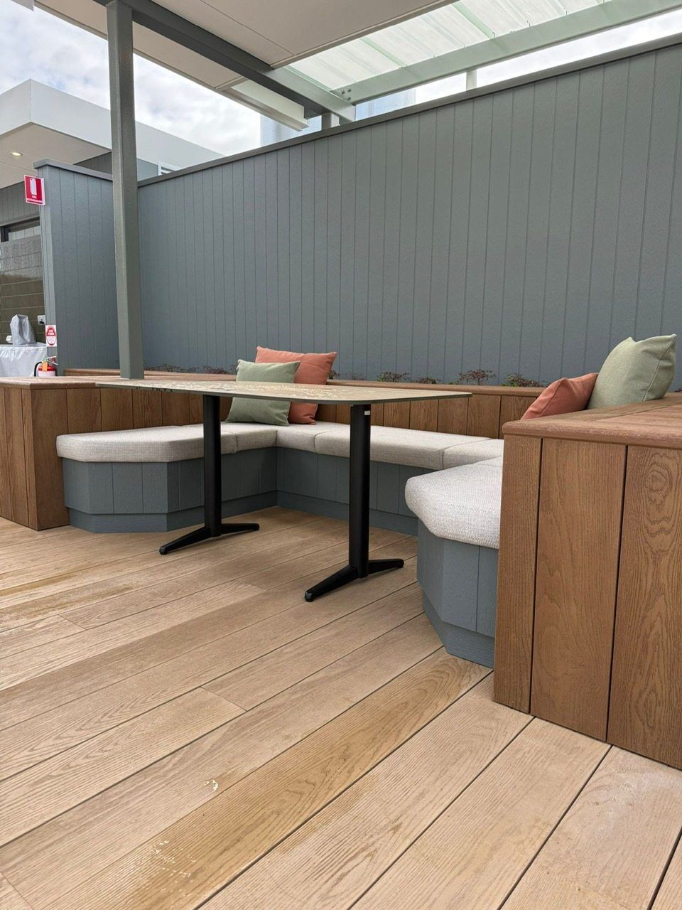 Modern outdoor patio seating with wooden tables, gray cushions, and a teal privacy wall