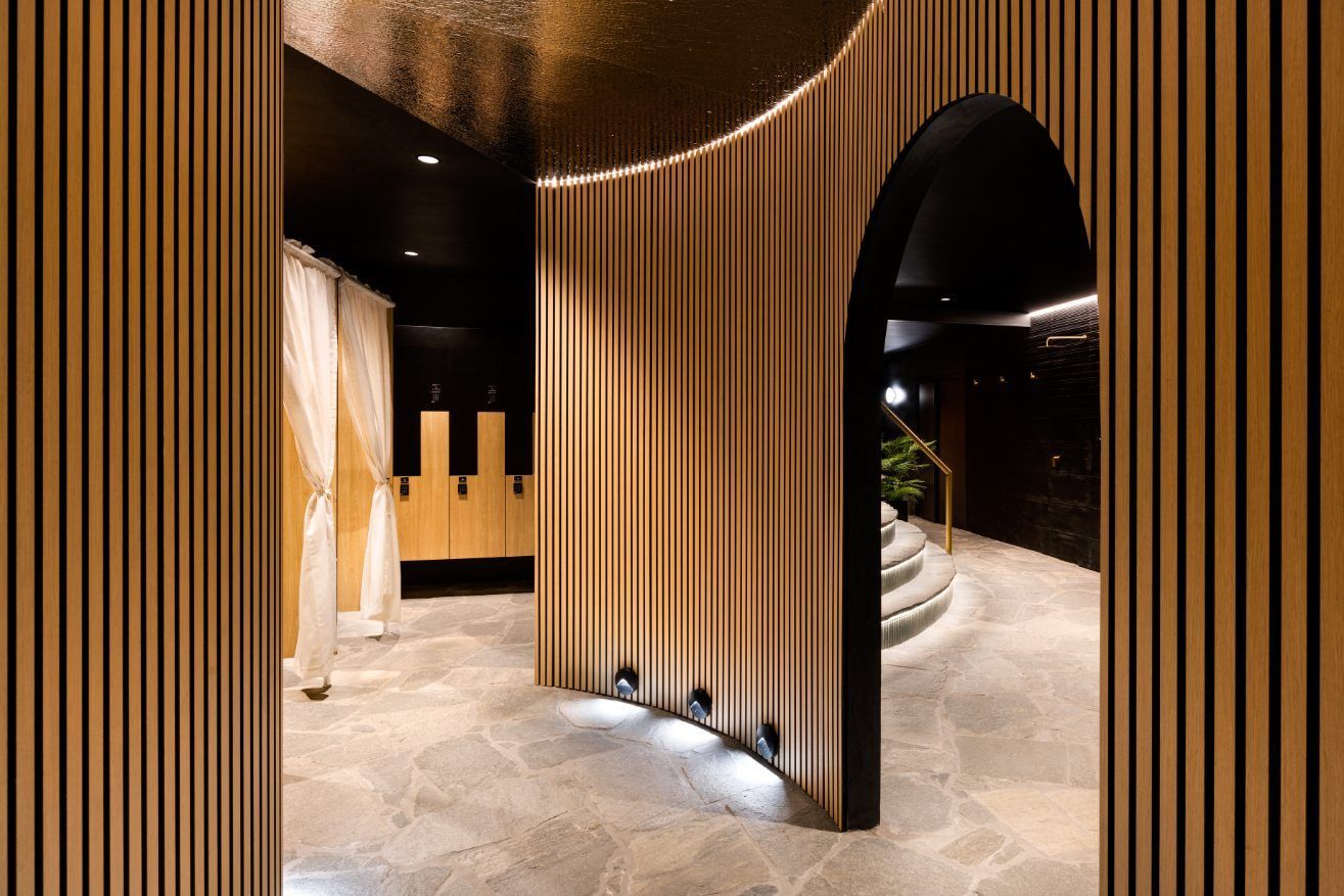 Modern interior with curved wooden slat walls, arched doorway, and a lit stone floor walkway